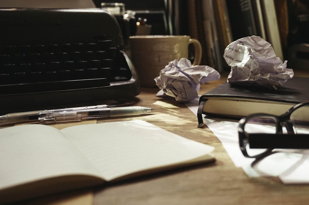 A writer's desk — typewriter, drafts, and an open notebook